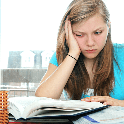 A female student experience test taking anxiety. She is looking at an open textbook. Her face rests in the palm of her right hand, and her face displays anxiety and frustration.